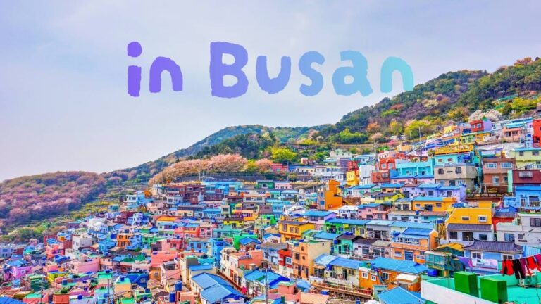 Colorful houses cascading down the hillside of Gamcheon Culture Village in Busan, with the text 'in Busan' overlaid in the sky.
